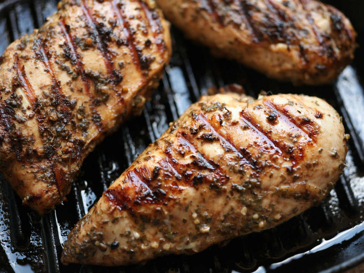 Seasoned chicken breasts grilling on a cast iron grill pan
