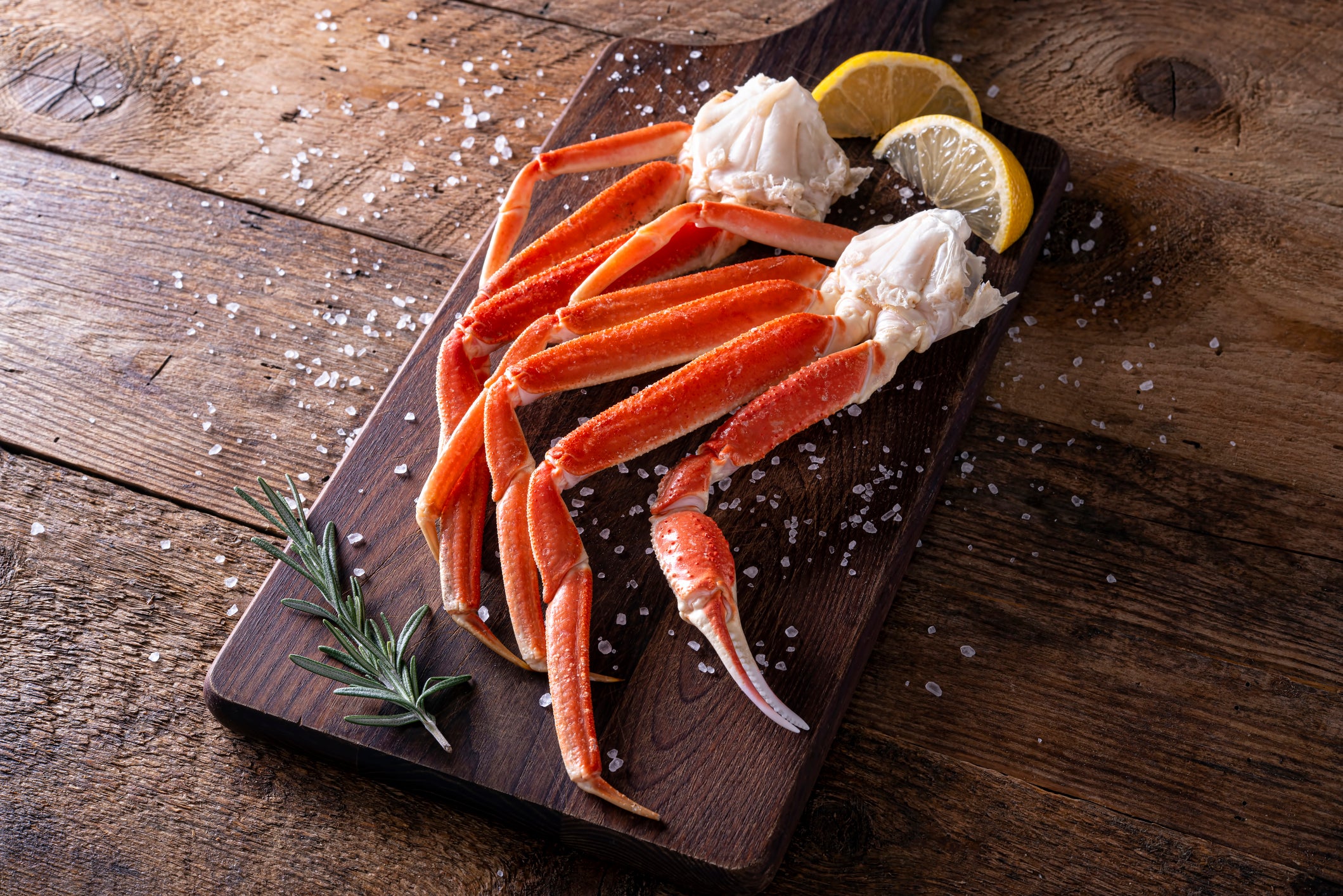Wild-caught crab legs on a wooden board with rosemary and salt