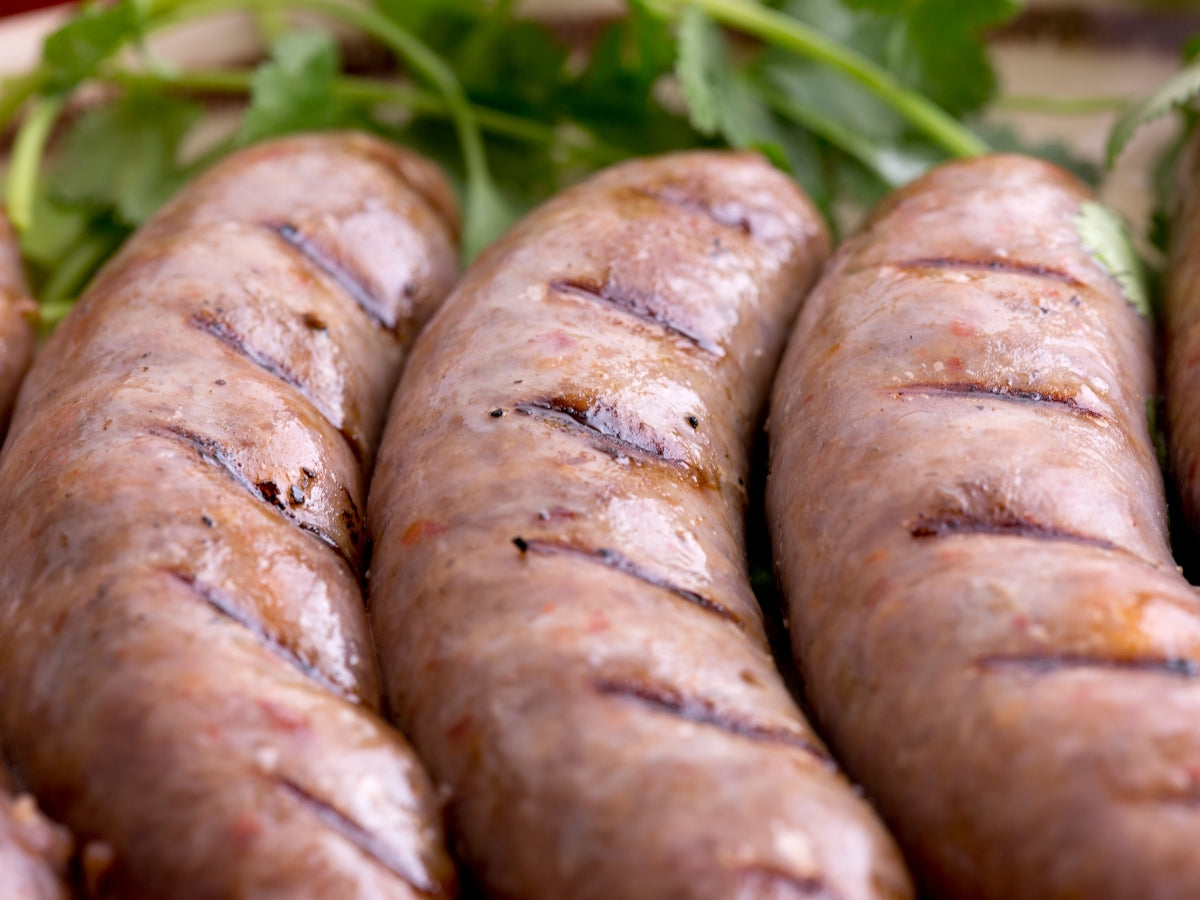 Grilled sausage links and a pork tenderloin on a herb-topped board